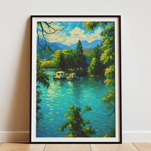 May include: Framed art print of a serene lake scene. The artwork features a vibrant turquoise lake surrounded by lush green trees and distant mountains under a blue sky. Two small boats are on the water. The print is in a black frame.