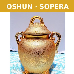 May include: A gold-colored, ornate ceramic jar with a lid. The jar features a floral pattern and gold accents on the handles and lid. The text "OSHUN - SOPERA" is displayed in a gold banner at the top of the image.