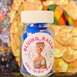 May include: A clear glass jar filled with blue spheres, topped with a white lid. The jar has a label with the words "BLUING BALLS" and an illustration of a woman in a turban. The text "ARIL * DIGO * WAJI" is also on the label.