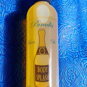 May include: A yellow body splash bottle with a black spray nozzle. The bottle has a champagne bottle graphic and the words "Paradis", "Body Splash", and "Champagne". It contains 8 Oz (237 ml) of product.