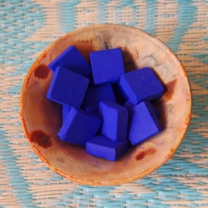 Pode incluir: Uma tigela redonda com tons de bege e castanho manchados, cheia com uma coleção de pequenos blocos quadrados de um azul real vibrante. A tigela tem um interior liso e curvo e um acabamento rústico e irregular com manchas castanhas.