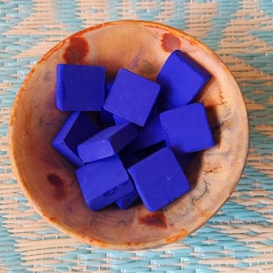 Peut inclure: Un bol en bois rempli d'objets carrés bleu vif. Le bol présente un grain de bois naturel avec des accents brun rougeâtre. Les objets sont disposés sur un tapis tissé bleu clair et blanc.