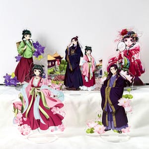 Puede incluir: Soportes acr&iacute;licos con personajes de estilo anime con vestimenta asi&aacute;tica tradicional. Las figuras est&aacute;n en varias poses, con ropa detallada y detalles florales. La paleta de colores incluye tonos de rosa, morado, verde y negro.