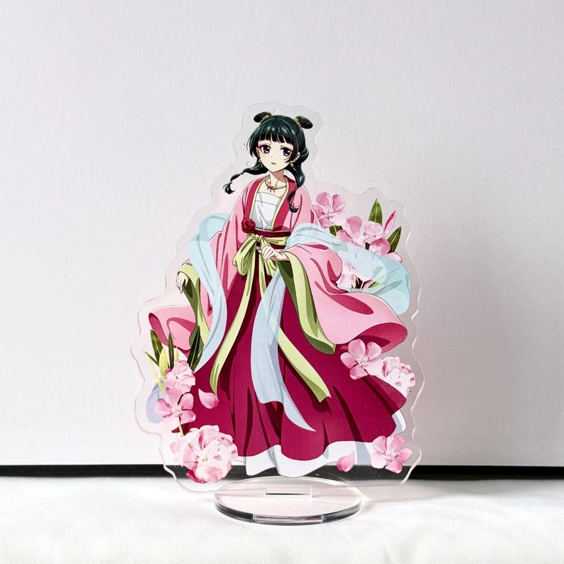 Puede incluir: Un expositor acr&iacute;lico transparente con un personaje femenino de anime con un vestido tradicional rosa y rojo, adornado con flores rosas. El personaje tiene cabello negro y est&aacute; sobre una base circular transparente.