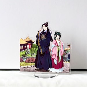 Puede incluir: Soporte acr&iacute;lico con dos personajes de estilo anime con vestimenta tradicional china. El personaje masculino viste una t&uacute;nica azul oscuro con detalles dorados, mientras que el personaje femenino lleva un atuendo rosa y rojo. El fondo representa un jard&iacute;n chino.