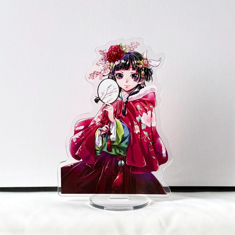 Puede incluir: Figura de pie de acr&iacute;lico transparente de una mujer con un atuendo tradicional rojo y estampado floral. Sostiene un peque&ntilde;o abanico y lleva una corona de flores. La figura tiene una base redonda.