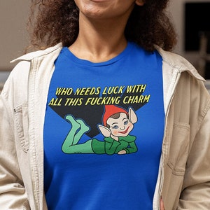 Puede incluir: Una camiseta azul real con una ilustración de un duende de dibujos animados y el texto "WHO NEEDS LUCK WITH ALL THIS FUCKING CHARM".