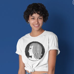 Pode incluir: Uma camiseta branca com uma ilustração em preto e branco de um rosto de mulher com um penteado estilizado. O rosto da mulher está de perfil e o cabelo está penteado em uma série de ondas.
