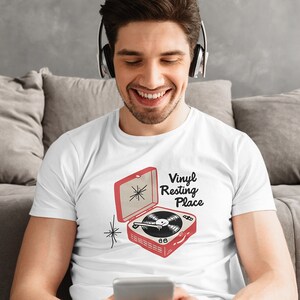 May include: White t-shirt with a red and black illustration of a vintage record player with the text "Vinyl Resting Place".