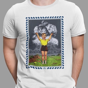 Könnte beinhalten: Ein weißes T-Shirt mit einem blauen und weißen Rand um eine Vintage-Illustration eines Jungen, der vor einer Pilzwolke steht. Der Text "Pop Cotton" befindet sich am unteren Rand der Illustration.