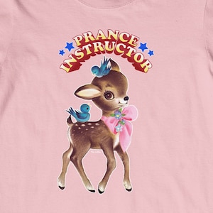 Puede incluir: Camiseta rosa con un gráfico de un cervatillo con pájaros azules y el texto "Prance Instructor" en una pancarta roja y blanca.
