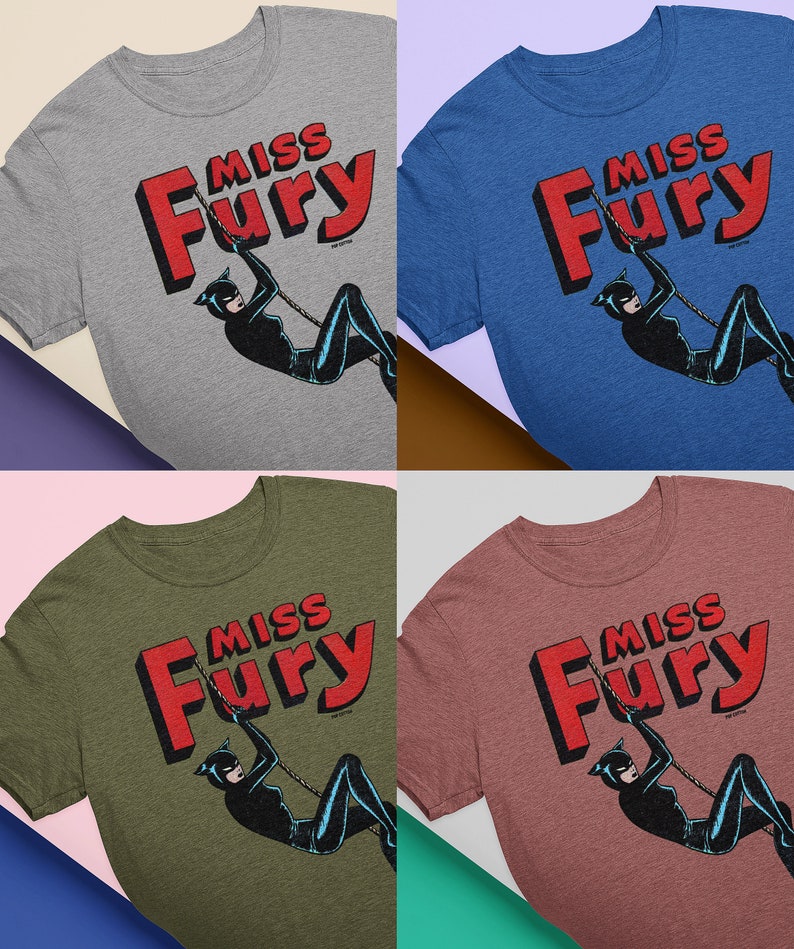 Puede incluir: Cuatro camisetas de diferentes colores con un gr&aacute;fico de estilo c&oacute;mic vintage de una mujer con un traje de gato negro balance&aacute;ndose en una cuerda. El texto "Miss Fury" est&aacute; en letras rojas sobre la mujer.