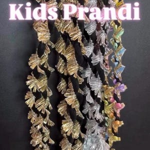 May include: A collection of decorative tassels featuring black braided cords adorned with metallic gold and silver fan-shaped embellishments, along with pastel-colored accents. The text Kids Prandi is overlaid in white across the center of the tassels.
