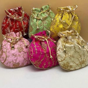 May include: A collection of six drawstring pouches in red, light green, yellow, light pink, magenta, and cream. Each pouch features intricate gold floral embroidery, a beaded drawstring closure, and small metallic bell accents at the ends.