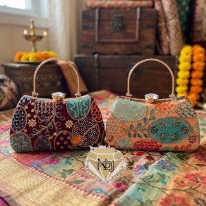 Puede incluir: Dos bolsos de mano estructurados con asas de metal dorado y cierres adornados con cristales. Un bolso es de color granate oscuro con bordados multicolores, mientras que el otro es de color melocotón con patrones florales y geométricos.