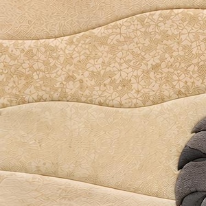 May include: A textured beige surface featuring wavy horizontal bands with intricate floral and geometric patterns embossed into the material. A portion of a dark grey, layered, fan-shaped element is visible on the lower right side of the frame.