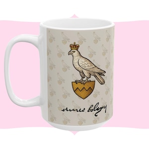 Könnte beinhalten: Weiße Keramiktasse mit einer detaillierten Illustration eines gekrönten Adlers auf einem goldenen Schild. Die Tasse hat ein sich wiederholendes Muster aus Adlern und Herzen auf beigem Hintergrund, mit Kursivschrift darunter.