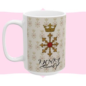 Könnte beinhalten: Weißer Keramikbecher mit einem sich wiederholenden Muster aus Kronen und Schneeflocken. Der Becher zeigt ein gold-rotes Emblem mit einer Krone und kursivem Text. Der Becher hat einen großen, gebogenen Griff.