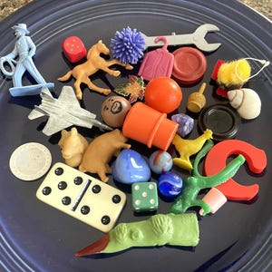 May include: A collection of small, colorful plastic toys and game pieces on a dark blue plate. Items include a cowboy figure, a horse, a jet, dice, a domino, and other miniature objects in various shapes and colors.