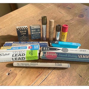 May include: A collection of vintage pencil lead refills and erasers in various rectangular boxes and cylindrical tubes. Brands include Scripto, Mark-All, and Sheaffer. The packaging features text such as Thin Lead, Thick Leads, and Smooth Writing Leads.