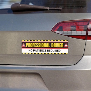 May include: A rectangular bumper sticker with the text "PROFESSIONAL DRIVER" above "NO PATIENCE REQUIRED". The sticker has a black and yellow striped border and a red and white central panel. It is affixed to the rear of a gray car.