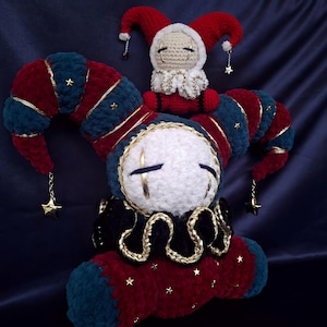 May include: A large plush jester doll with a white face, closed eyes, and a multi-pointed hat in red and teal velvet, accented with gold stars and dangling star charms. A smaller matching jester doll sits atop the larger one's head.