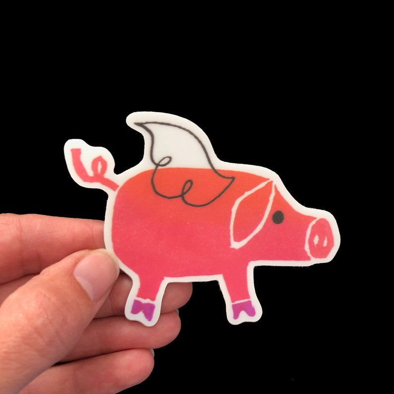 May include: A pink pig sticker with a white wing. The pig has a black eye and a black nose.