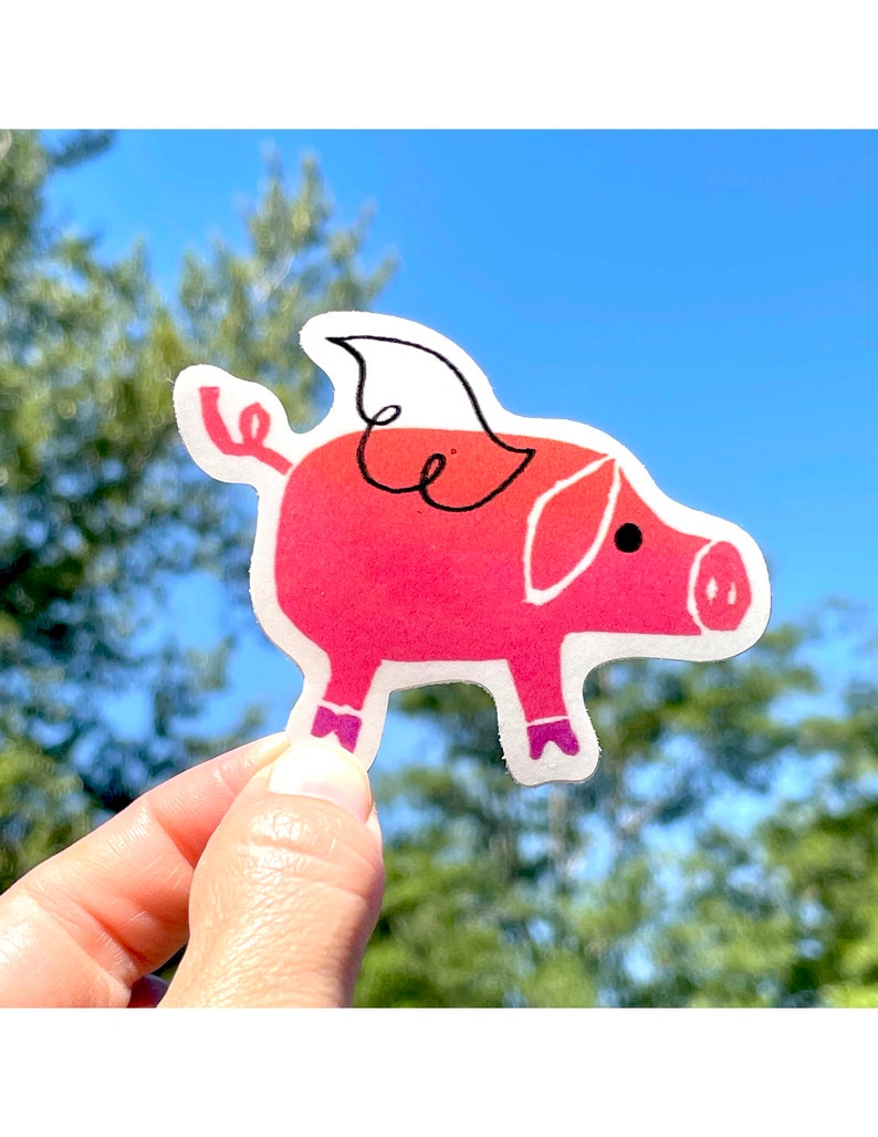 May include: A pink pig sticker with a white wing and purple shoes. The pig is holding a curled tail in its mouth.
