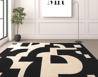 May include: A rectangular area rug featuring a bold, high-contrast pattern of large, interlocking black and cream-colored geometric shapes. The design consists of thick, curved, and straight lines that create an abstract, puzzle-like composition.