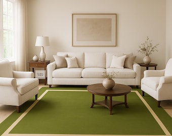Puede incluir: Una alfombra rectangular grande con un campo central de color verde oliva sólido enmarcado por un borde ancho de color beige claro. La alfombra está colocada sobre un suelo de madera clara en una sala de estar, creando un contraste de color.