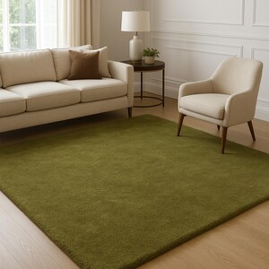 May include: A rectangular area rug featuring a solid olive green color with a dense, short-pile texture. The rug is positioned flat on a light-toned wooden floor, covering a large surface area with clean, straight edges and a uniform appearance.