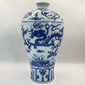 Peut inclure: Un vase en céramique blanc et bleu avec un couvercle. Le vase présente un motif de dragon bleu détaillé, des nuages et des vagues. La base a un motif géométrique. Le couvercle et le bord sont de couleur bleu clair.