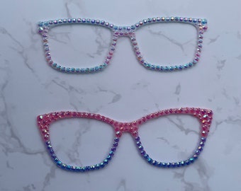 May include: Two pairs of rhinestone glasses. The top pair is light blue and the bottom pair is pink and blue.