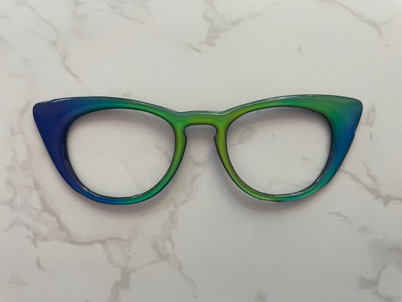 May include: A pair of cat-eye glasses with a gradient blue to green frame.