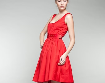 Puede incluir: Un vestido rojo vibrante con un corpiño ajustado y una falda acampanada. El vestido presenta un cinturón rojo a juego que ciñe la cintura. La modelo lleva tacones altos grises. Un estilo clásico y elegante.