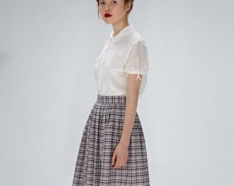 May include: A woman wearing a white collared blouse with a plaid skirt and white heels.