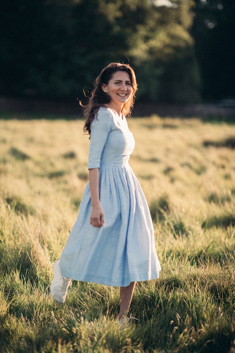 A woman in a simple blue wedding dress smiles as she walks through a sunlit field, embodying joy and tranquility.