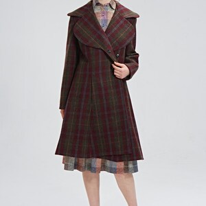May include: A long, burgundy and green plaid coat with a large, folded collar. The coat has a button closure and a slightly flared skirt.