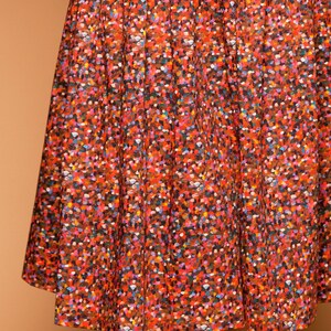 May include: A red skirt with a colorful confetti print. The skirt is made of a lightweight fabric and has a flowy silhouette.