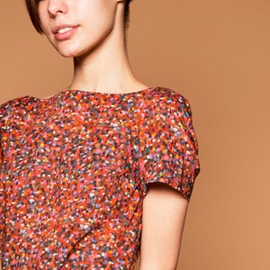 May include: A woman wearing a short-sleeved red dress with a colorful confetti print.