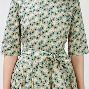 May include: A beige dress with a floral print featuring small blue flowers. The dress has a boat neck and a self-tie sash.
