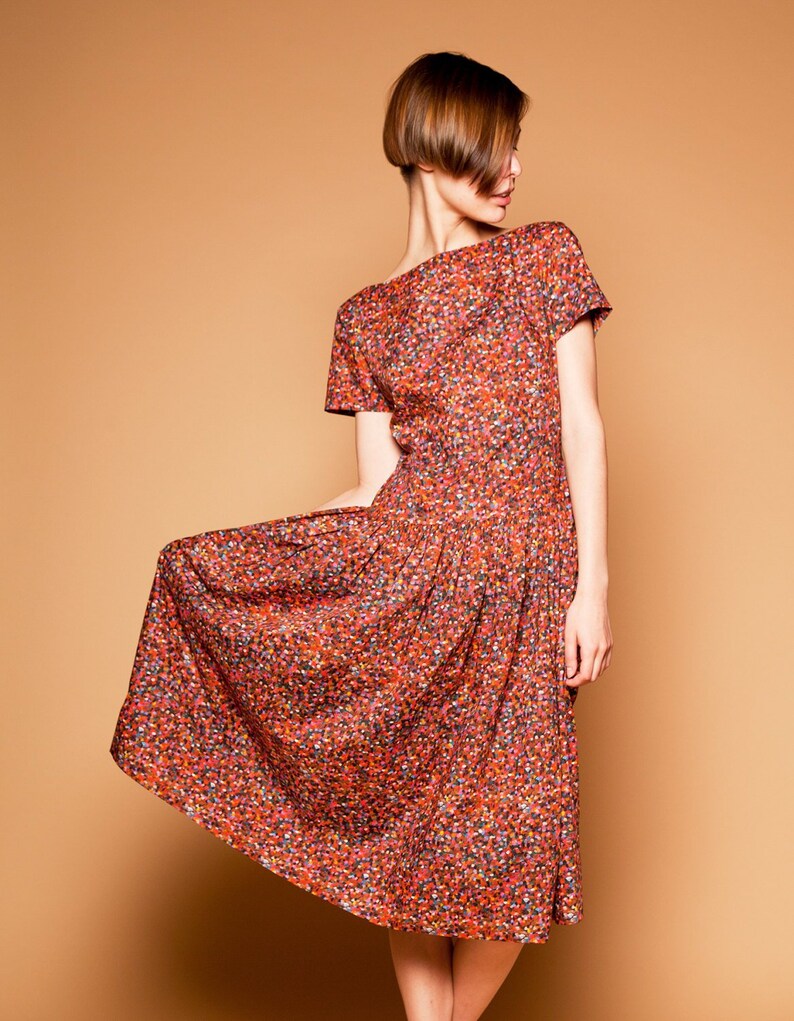 May include: A woman wearing a short-sleeved, knee-length dress with a red, orange, and black floral print. The dress has a scoop neckline and a gathered skirt.