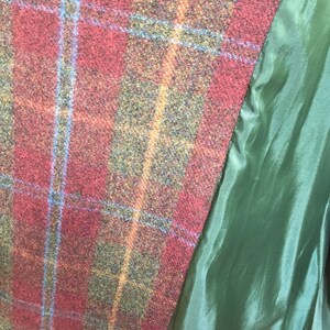 May include: Close-up of a red, green, and blue plaid fabric with a green lining. The fabric has a textured, woven appearance.