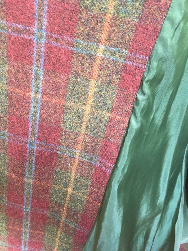 May include: Close-up of a red, green, and blue plaid fabric with a green lining. The fabric has a textured, woven appearance.