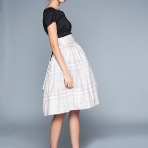 May include: A woman wearing a black top and a white and beige plaid skirt. She is wearing black high heels.