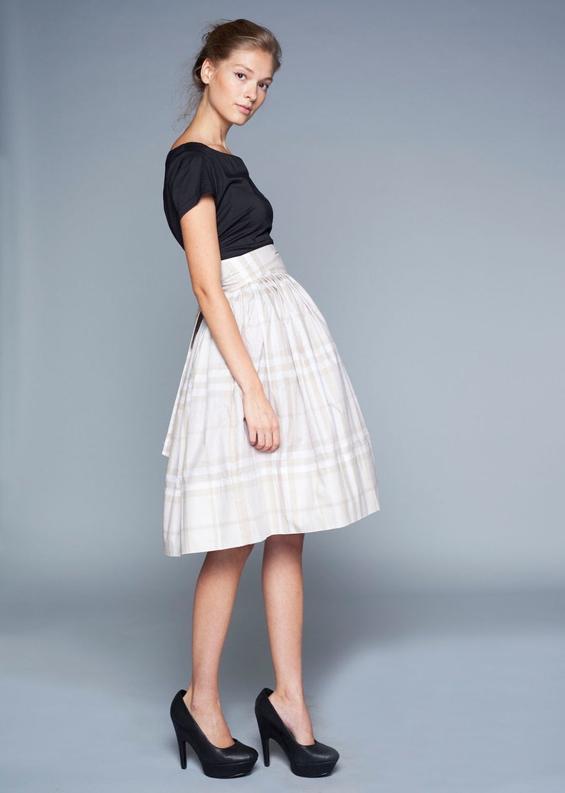 May include: A woman wearing a black top and a white and beige plaid skirt. She is wearing black high heels.