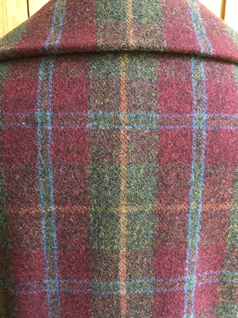 May include: Close-up of a burgundy, green, and blue plaid fabric. The fabric has a fuzzy texture and is woven in a plaid pattern.