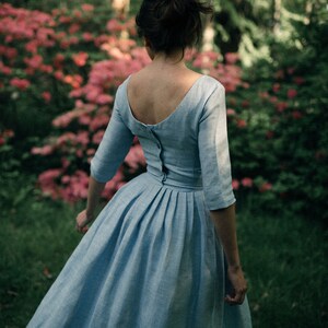 A woman in a blue linen dress walks gracefully through a lush forest.
