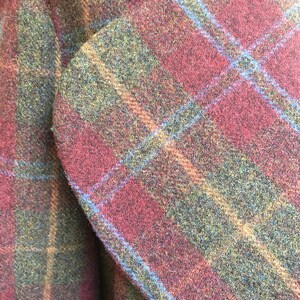 May include: Close-up of a red, green, and blue plaid fabric. The fabric has a fuzzy texture and is woven in a plaid pattern.