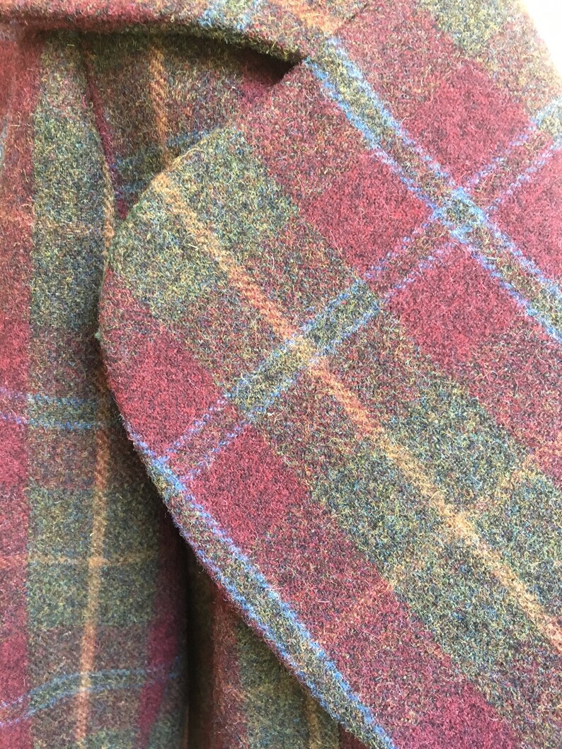 May include: Close-up of a red, green, and blue plaid fabric. The fabric has a fuzzy texture and is woven in a plaid pattern.